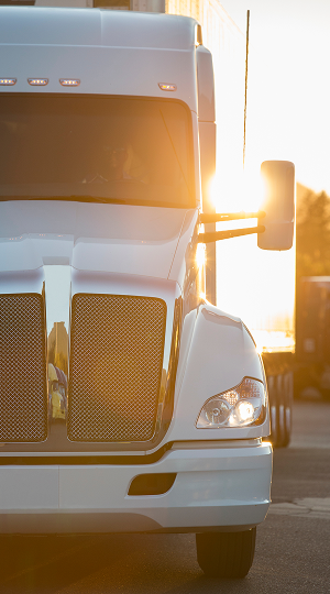 Front of a white semi-truck with a mirror reflecting the sunlight
